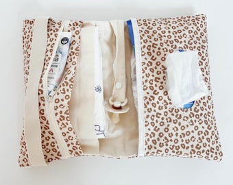 May include: A brown and beige leopard print changing mat with a zipper closure. The mat is open and contains a white diaper, a white pacifier, and a white tissue pack.