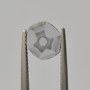 May include: A clear glass bead with a faceted design, held by tweezers.