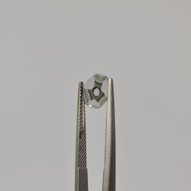 May include: A clear glass lens with a star-shaped pattern is held by tweezers. The lens has a small hole in the center.