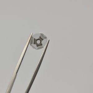 May include: A clear glass gem with a star-shaped pattern inside, held by silver tweezers.