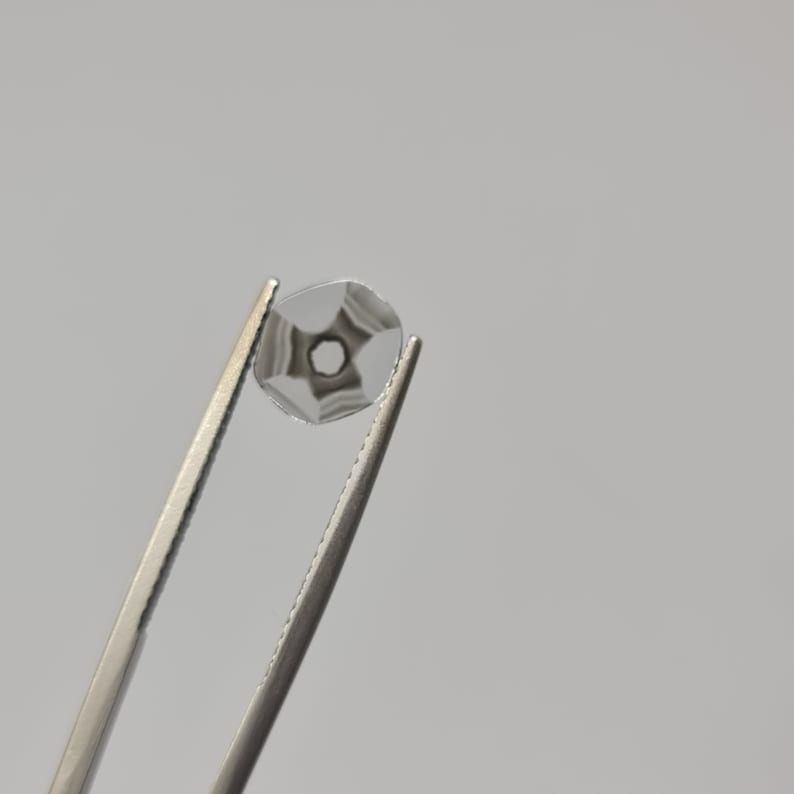 May include: A clear glass gem with a star-shaped pattern inside, held by silver tweezers.