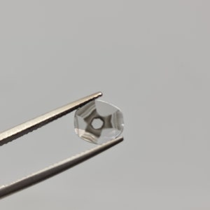 May include: A clear, faceted, round gemstone with a hole in the center, held by tweezers.