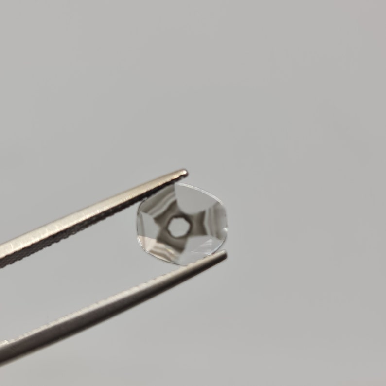 May include: A clear, faceted, round gemstone with a hole in the center, held by tweezers.