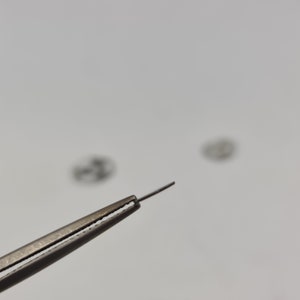 May include: A close-up of a pair of tweezers holding a small, thin, silver-colored object. The object is out of focus, but the tweezers are in sharp focus.
