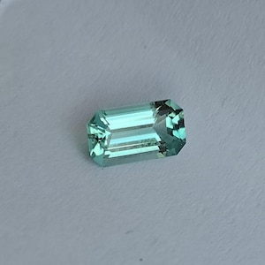 May include: A light green emerald cut gemstone with a rectangular shape.