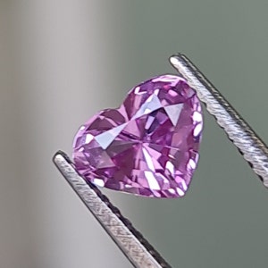 May include: A heart-shaped, pink gemstone with facets, held by tweezers.