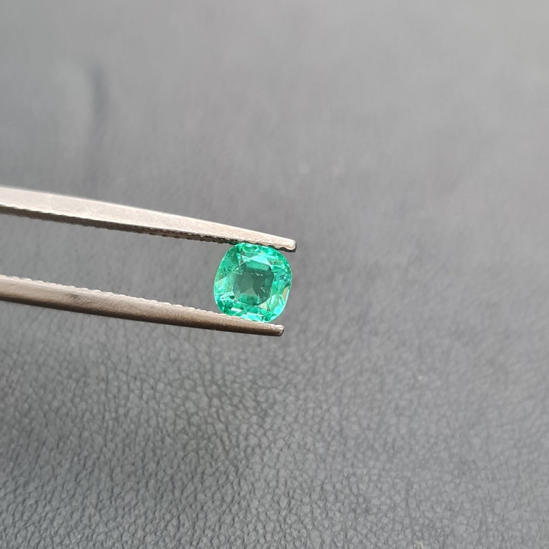 Puede incluir: Una gema de esmeralda verde vibrante sostenida en pinzas. La esmeralda tiene un corte coj&iacute;n y es de un hermoso tono verde.