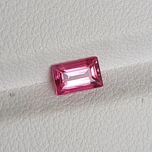May include: A pink rectangular gemstone with a faceted cut.
