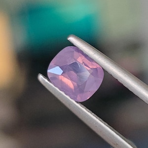 May include: A light purple gemstone with a cushion cut, held by tweezers.