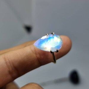 May include: A pearlescent iridescent gemstone ring with a teardrop-shaped stone set in a silver band.