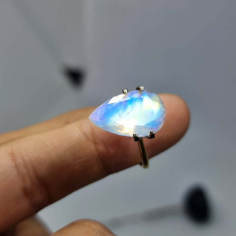 May include: A pearlescent iridescent gemstone ring with a teardrop-shaped stone set in a silver band.