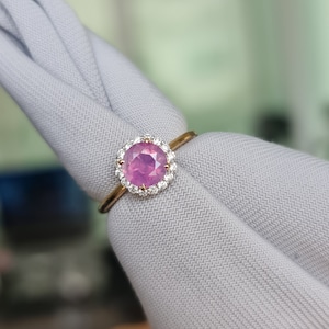 May include: A pink gemstone ring with a halo of smaller diamonds set in gold.