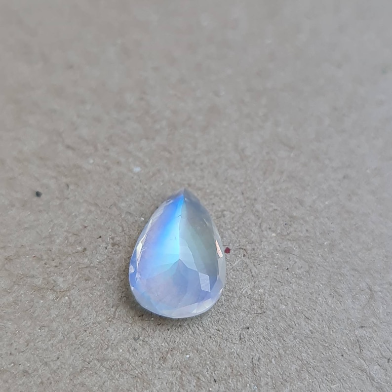 May include: A pearlescent teardrop-shaped moonstone gemstone with a blue iridescent sheen.