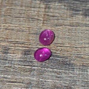 May include: Two pink oval-shaped gemstones with a star-shaped pattern inside.