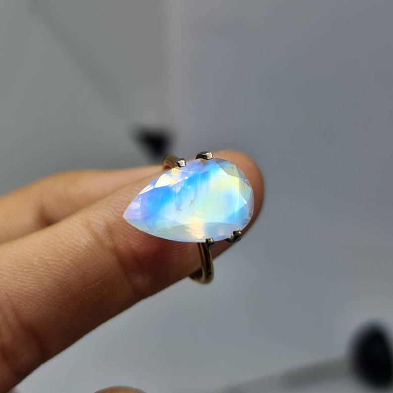 May include: A pearlescent iridescent gemstone ring with a teardrop-shaped stone set in a silver band.