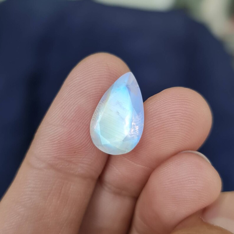 May include: A teardrop-shaped moonstone gemstone with a pearlescent sheen and iridescent rainbow colors.