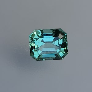 May include: A green gemstone with a rectangular emerald cut.