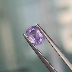 Puede incluir: Una piedra preciosa ovalada de color lila claro sostenida en unas pinzas.