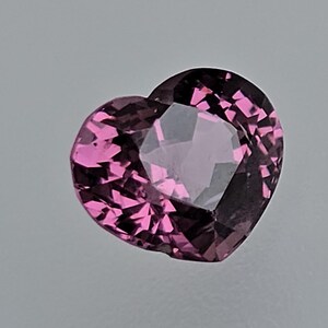 May include: A heart-shaped pink gemstone with a faceted cut. The gemstone is set in a clear, faceted setting.