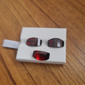 May include: Three red gemstone cabochons, two are rectangular and one is oval, displayed on a white background.