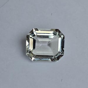 May include: A clear, faceted, emerald-cut gemstone with a rectangular shape.
