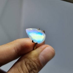 May include: A pearlescent iridescent gemstone ring with a teardrop-shaped stone set in a gold band.