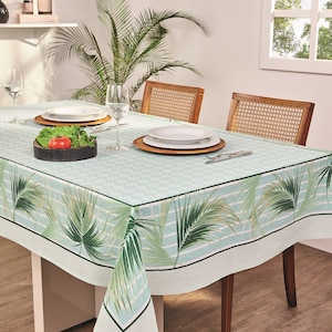 May include: A rectangular tablecloth with a light blue and white checkered pattern, featuring a border with green palm fronds. The table is set with plates, glasses, and a wooden bowl of vegetables. The table is 60 inches long.