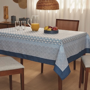 以下が含まれることがあります： 青と白の波模様の長方形のテーブルクロスが木製のテーブルに置かれています。テーブルにはオレンジジュースのピッチャー、果物、グラスが置かれています。織りのペンダントライトが上に吊り下げられています。