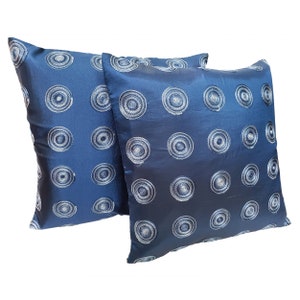 May include: Two square navy blue cushions. Each cushion has a repeating pattern of embroidered white concentric circles. The cushions have a shiny, satin-like texture, adding a touch of elegance. Home decor.
