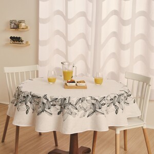 May include: A round dining table set for a meal. The table is covered with a white tablecloth featuring a black and gray floral design. Two white chairs are positioned around the table, with a pitcher of juice and glasses.