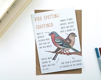 May include: A greeting card featuring a Chaffinch bird spotting guide with illustrations of a male and female bird on a branch. The text reads: BIRD SPOTTING: CHAFFINCH, MALE IS BRIGHTLY COLOURED WITH GREY-BLUE CAP AND RED BREAST, FEMALE IS MORE SUBDUED, BUFFISH WHITE AND GREY WITH A BROWN CAP, OBVIOUS WHITE BARRING ON WINGS AND SIDES OF TAIL, FIND THEM IN OPEN WOODS OR FORAGING ON THE GROUND.