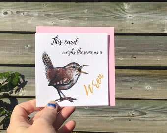 May include: A square greeting card with a light pink envelope featuring a watercolor illustration of a brown wren with its beak open. The text on the card reads, This card weighs the same as a Wren, with the word Wren printed in gold script.