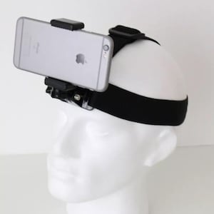 Op de afbeelding: Een zwart hoofdband met een telefoonhouder eraan bevestigd. De telefoonhouder houdt een zilveren smartphone vast. Het hoofdband wordt gedragen op een wit mannequinhoofd.