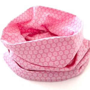 Könnte beinhalten: Rosafarbener Stoff-Halswärmer mit weißem Blumenmuster. Der Stoff ist gefaltet, um einen warmen und gemütlichen Halswärmer zu schaffen.