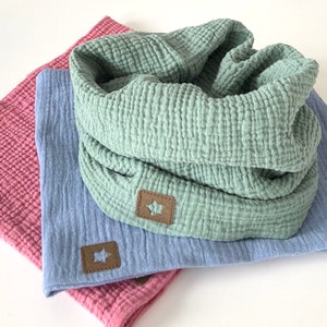 Könnte beinhalten: Drei Stoffquadrate in verschiedenen Farben: hellblau, grün und rosa. Jedes Quadrat hat einen braunen sternförmigen Patch, der darauf genäht ist.