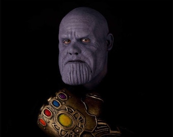 Può includere: Un primo piano di Thanos, un personaggio immaginario dell'Universo Cinematografico Marvel, con il viso viola e un guanto dorato con le gemme dell'infinito.