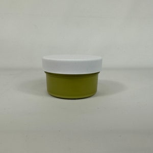 Könnte beinhalten: Ein kleines, rundes Glas mit einem weißen Deckel. Das Glas ist mit einer hellgrünen Substanz gefüllt.