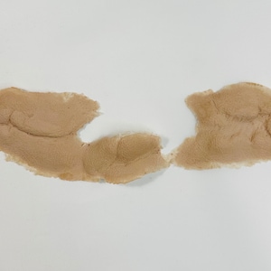 May include: A close-up of a light brown, textured, fabric patch with a torn edge.