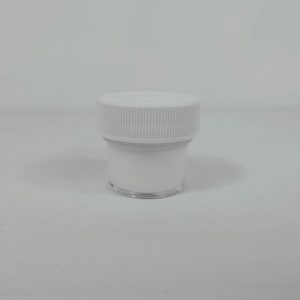 Puede incluir: Un tarro de plástico blanco con una tapa blanca. El tarro está vacío y tiene una base de plástico transparente.