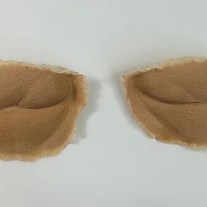 May include: Two brown, textured, fabric pieces shaped like lips. The pieces are slightly curved and have a rough, uneven texture.