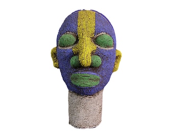May include: A beaded sculpture of a human head with a blue, yellow, and green face. The sculpture is made of small, colorful beads.