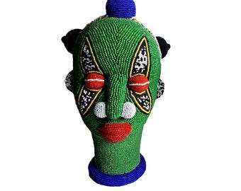 May include: A green beaded head sculpture with a blue beaded crown, black beaded hair, and a colorful beaded face.