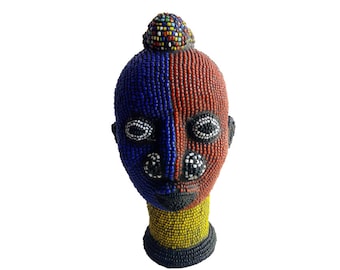 May include: A beaded sculpture of a human head with a blue and red face and a yellow beaded neck. The head is decorated with colorful beads and has a small, colorful beaded crown on top.