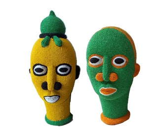 May include: Two beaded sculptures of human heads. One head is yellow with a green crown and the other is green with an orange trim.