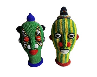May include: Two beaded sculptures of human heads with colorful patterns and designs. The sculptures are made of green, yellow, red, blue, white, and black beads.