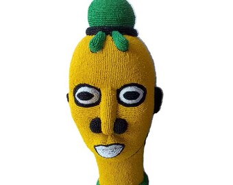 May include: A beaded sculpture of a human head with a green crown. The head is yellow, the eyes are black and white, and the nose and mouth are black.