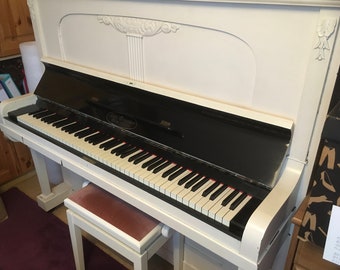 May include: A white upright piano with a black keyboard and a black and white bench. The piano has a black finish on the top and a white finish on the body.