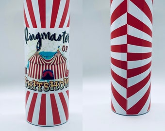 May include: A white tumbler with red and white stripes. The tumbler has a graphic of a circus tent with the text "Ringmaster of the Shitshow".