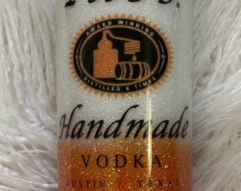 Könnte beinhalten: Ein weißer und orangefarbener Glitzerbecher mit dem Text "Tito's Handmade Vodka Austin Texas" und einem schwarz-weißen Logo mit dem Text "Award Winning Distilled 6 Times".