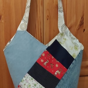 May include: A blue and white patchwork tote bag with a floral pattern and a deer print. The bag has two long straps.
